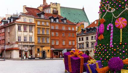 Famous Castle Square in Warsaw's Old Town in winter, huge Christmas tree on right side, colourful houses and buildings all around